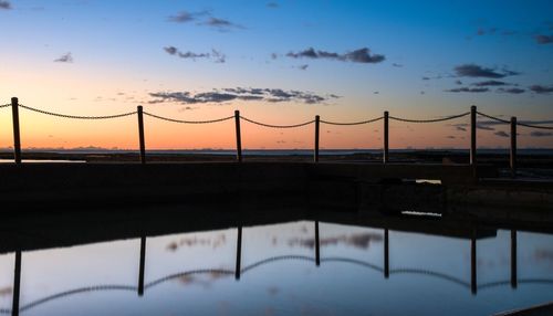 Bridge over swimming pool against sky during sunset