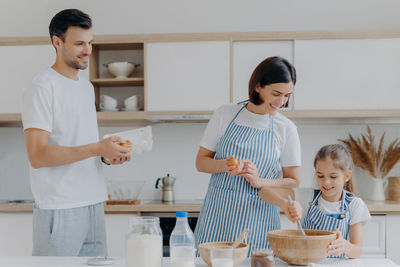 Man looking at mother and daughter preparing food in kitchen