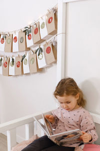 Mather with toddler child reading book or photo album on christmas eve near eco advent calendar in