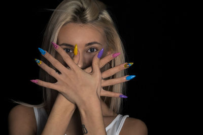 Portrait of young woman showing her nail polish art against black background