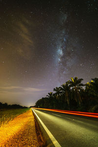 Road by trees against sky at night
