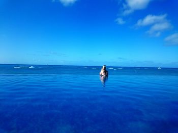 Rear view of woman in infinity pool by sea against sky
