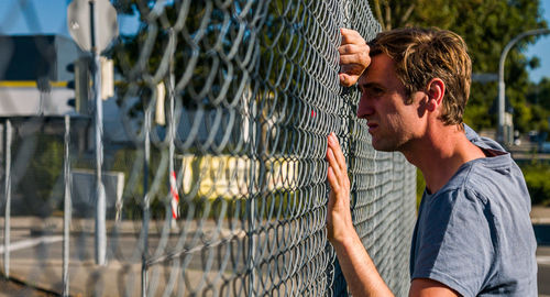 Sad caucasian man leaning forehead against fence. profile view. portrait.