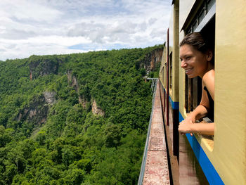 Smiling woman looking through train window against sky