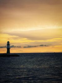 Lighthouse by sea against cloudy sky during sunset