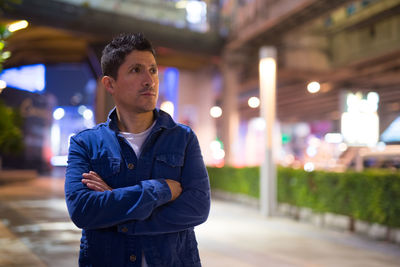 Portrait of young man standing against illuminated city at night