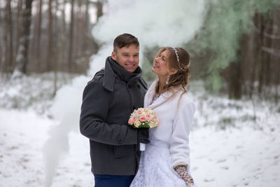 Portrait of groom with bride standing at forest during winter