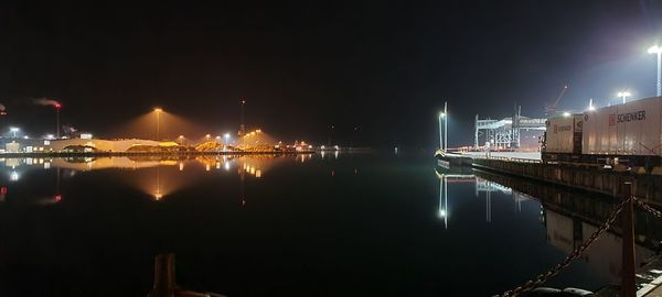 Illuminated buildings by sea against sky at night