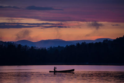 Silhouette man on boat sailing in lake against sky during sunset