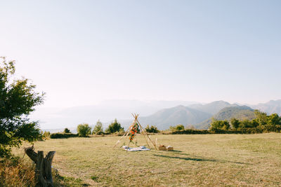 Rear view of woman walking on field against clear sky