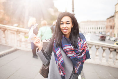 Portrait of smiling young woman standing on mobile phone in city