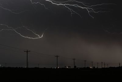 Silhouette of electricity pylon against sky at night