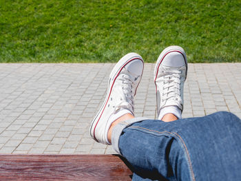 Woman feet in white sneakers on grass lawn. rest on bench in urban park. enjoying sunlight outdoors.