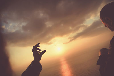 Silhouette hand against sky during sunset