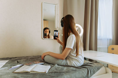 Teenage girl in headphones in front of the mirror takes selfie, admires. reflection