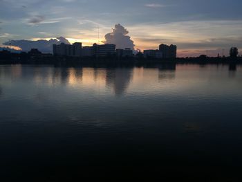 Silhouette buildings by river against sky during sunset
