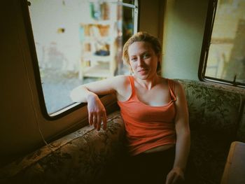 Portrait of woman sitting on window at home