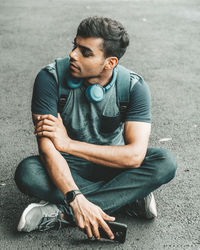 Young man looking away while sitting on road in city