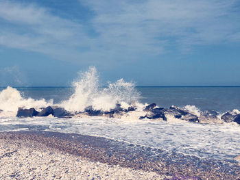 Waves splashing on shore against sky