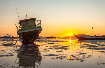 Fishing boat on beach against sky during sunset