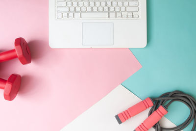 Directly above shot of laptop by dumbbells and jump rope on colorful table