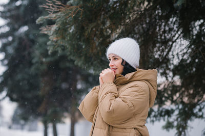 A nice woman with a white hat and warms her hands. it stands in the city in winter under the snow
