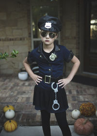 Portrait of confident girl in police costume with hands on hip standing against house during halloween