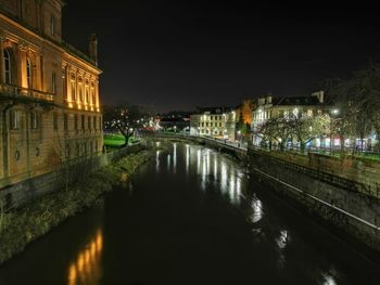 Bridge over river amidst illuminated buildings in city at night