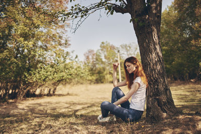 Portrait of smiling young woman sitting on tree trunk
