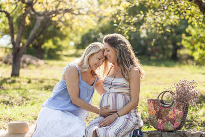 Mother with pregnant daughter sitting at park