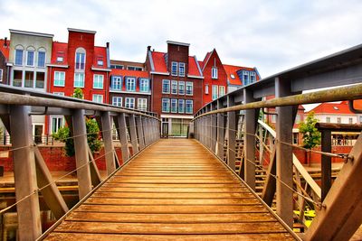 Footbridge over footpath amidst buildings against sky