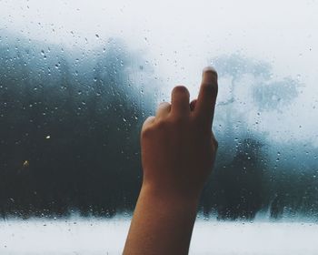 Cropped hand of person touching window with raindrops