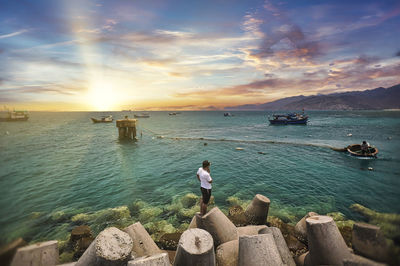 High angel view of man standing on rocks by sea against sky during sunset