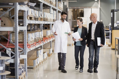 Full length of engineer explaining machine part to business people in factory