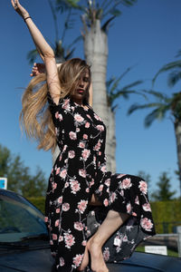 Full length of woman crouching on vehicle hood against sky