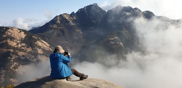 Man sitting on rock against mountains