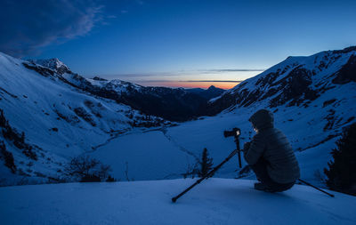 Rear view of man photographing on snowcapped mountain at dusk