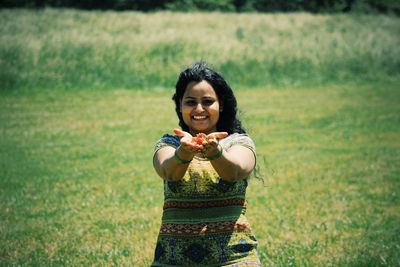 Portrait of woman holding flowers with cupped hands kneeling on grassy field