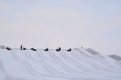 People on tobogganing on snow covered land against sky
