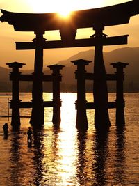 Silhouette wooden posts in sea against sky during sunset