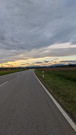 Road amidst field against sky during sunset