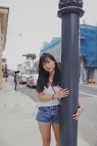 Portrait of young woman standing by pole against building