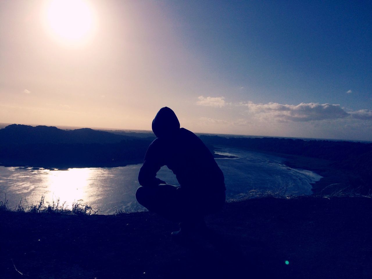 SILHOUETTE MAN SITTING ON BEACH AGAINST SKY