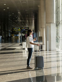 Young woman standing with baggage near the airport window waiting for the flight