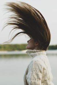 Close-up of young woman tossing hair against sky