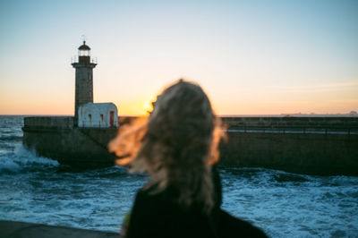 Lighthouse on beach against sky at sunset