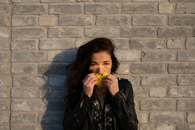 Portrait of woman smelling flower against wall outdoors
