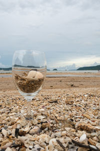 Close-up of wineglass on beach against sky