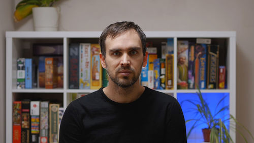 A handsome middle-aged caucasian man in a black sweatshirt in a room against a rack of board games