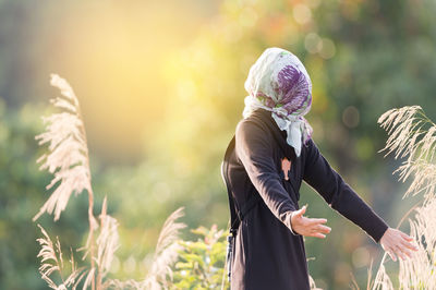 Woman with arms outstretched standing by plants